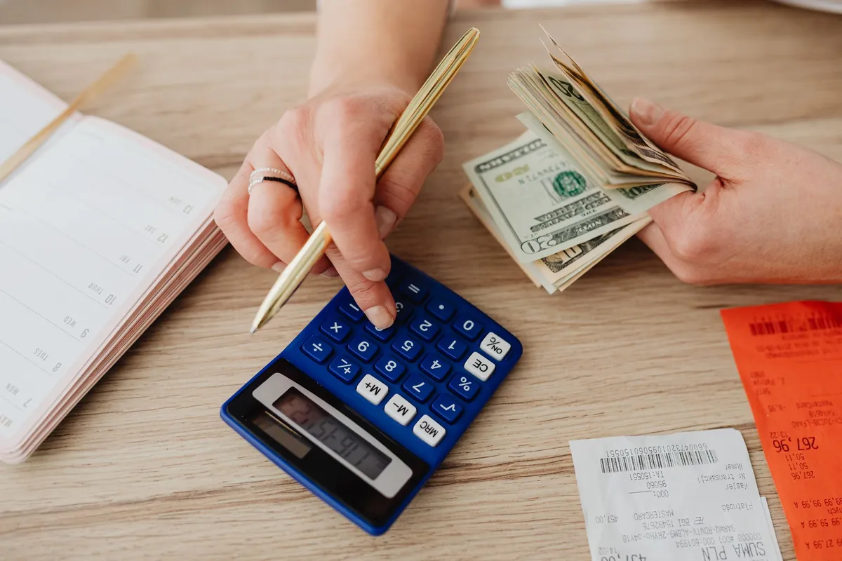 Mãos contando notas e usando calculadora - reduzir inadimplência com cobrança automatizada na Poupar AI
